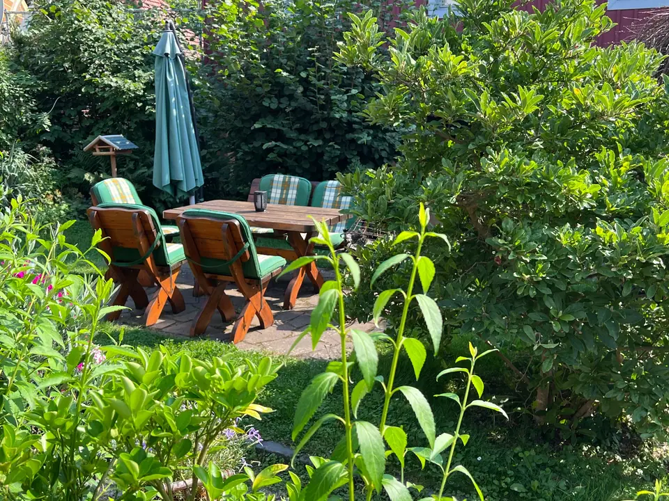 Sitzplatz im Garten: Gemütliche Holzmöbel zwischen Blumen und Sträuchern, gleich am Haus.