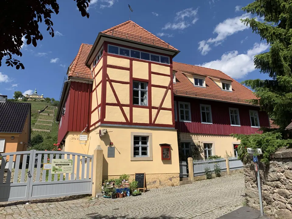 Das Retzschgut von der Weinbergstraße aus: Fachwerkturm und ochsenblutrote Holzfassade, links oben am Hang das Spitzhaus